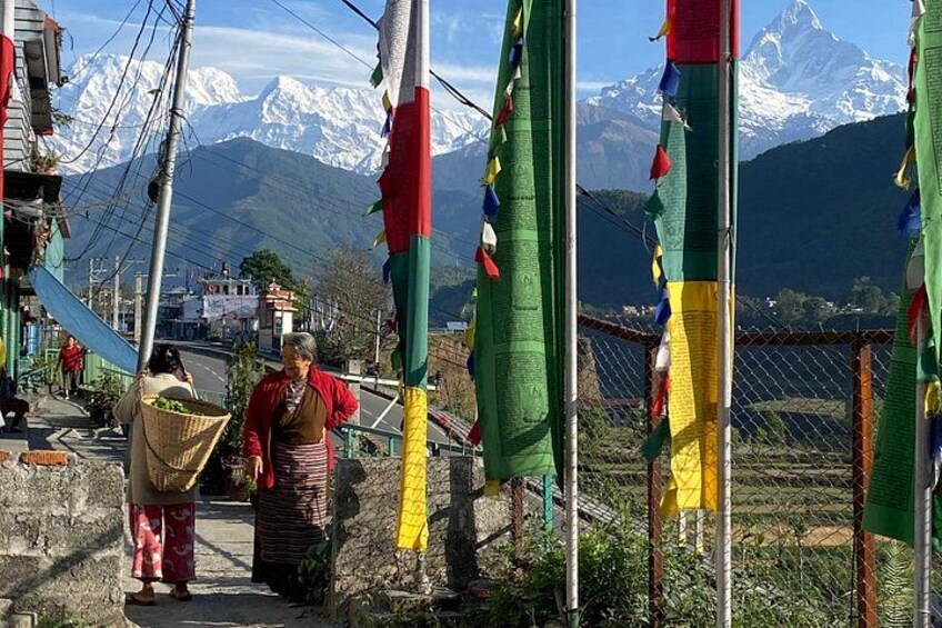 A mountainous landscape with snow-capped peaks, a person carrying a basket, and colorful prayer flags. 2