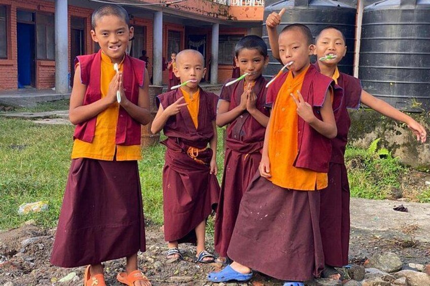 Children in maroon and orange robes standing on a rocky path with buildings in the background. 2