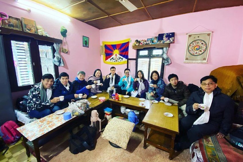 A group of people sitting around a table in a room with pink walls, a flag, and various decorations. 5
