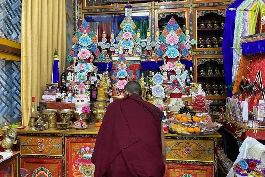 A monk in a maroon robe performing a ritual in a richly decorated room with colorful prayer flags and traditional Tibetan artifacts. 3