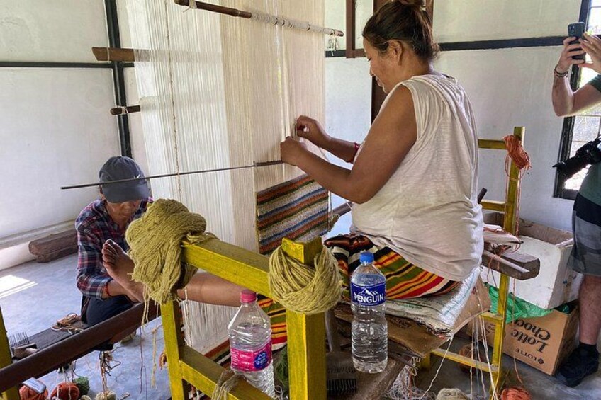 A person weaving on a loom, with a bottle and a box nearby. 5