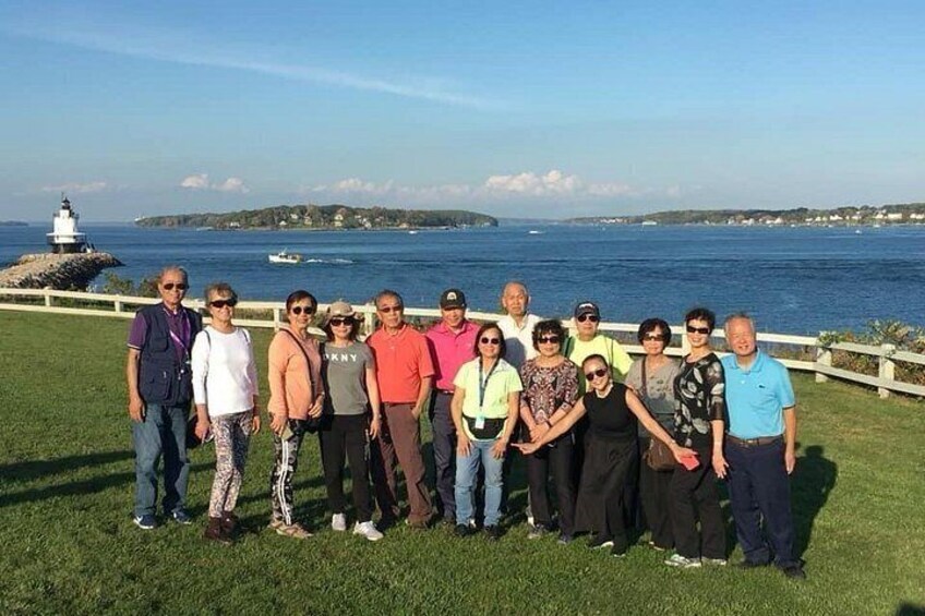 Un groupe de personnes se tient sur l’herbe, près d’un phare et de l’océan. 2
