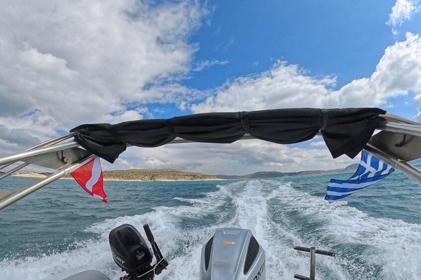 A boat speeding through water with a red and blue flag, a black canopy, and a mountainous coastline in the background. 2