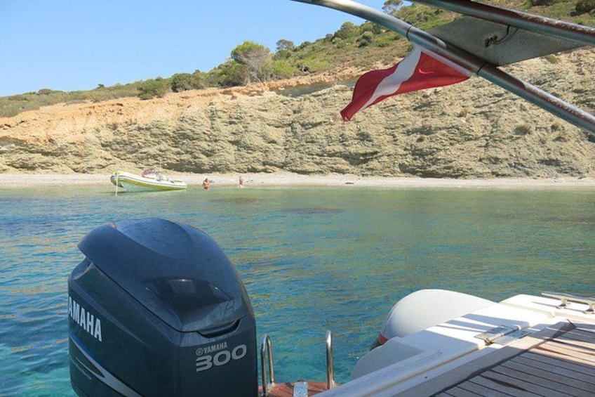 Een boot met een Yamaha 300 buitenboordmotor, kalm water, een zandstrand en een rotsachtige klif op de achtergrond. 2