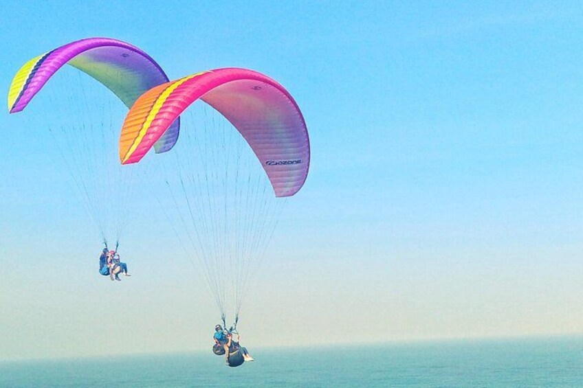 Drie paragliders met kleurrijke parachutes boven een wateroppervlak. 1