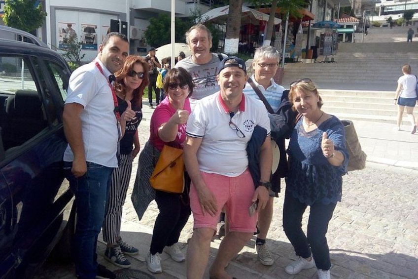 Un grupo de personas posando para una foto en un entorno urbano, con una zona pavimentada y edificios al fondo. 2