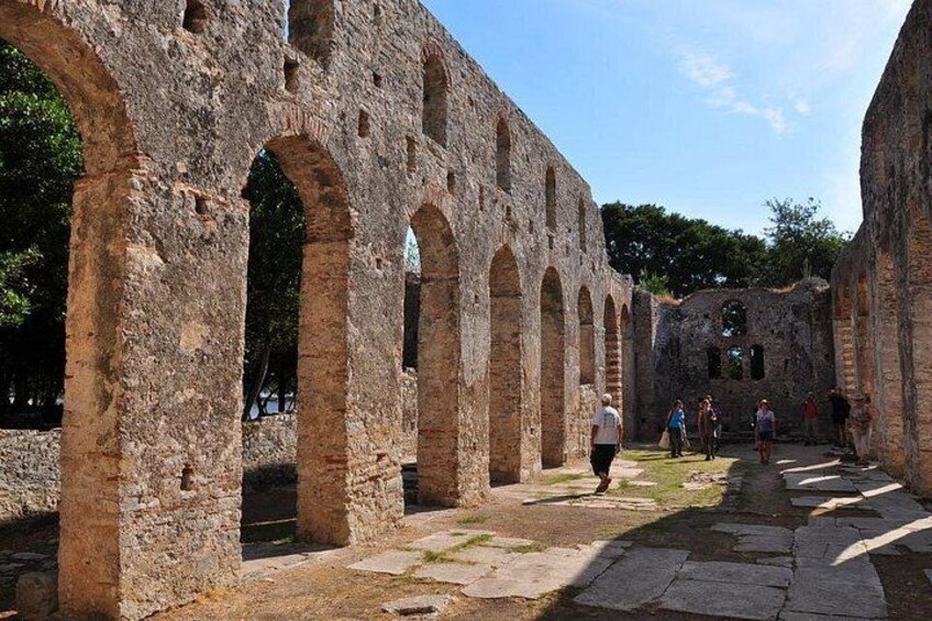 Una antigua estructura de piedra con arcos y columnas, un camino y visitantes. 4