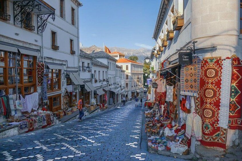 A cobblestone street lined with shops displaying colorful textiles. 2