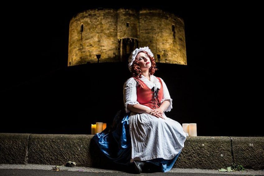 A person in historical costume sitting on a stone ledge with a castle in the background. 3