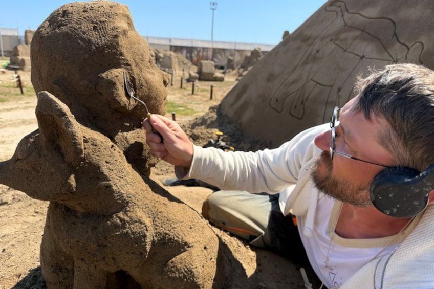 Una persona observa una gran escultura de arena que representa un busto. 2