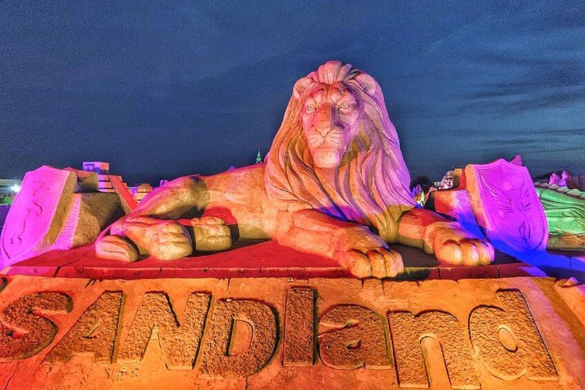 A large lion sculpture with the word 'SANDLAND' carved into the base. 1