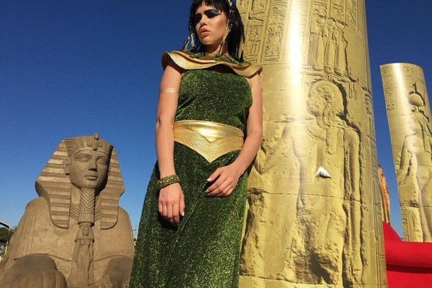 A person in a green dress standing in front of a large golden statue with hieroglyphics. 5