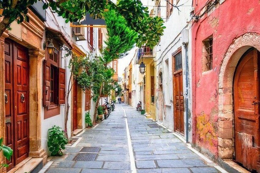 A narrow street lined with colorful buildings, stone pavement, and green plants. 1