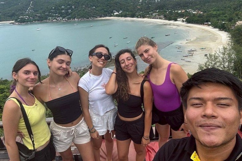 En gruppe mennesker står ved en kyststrækning med en strand og både i baggrunden. 3