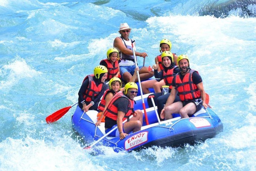 Un groupe de personnes à bord d’un radeau bleu, portant des gilets de sauvetage rouges, et qui navigue à travers des rapides aux eaux tumultueuses. 1