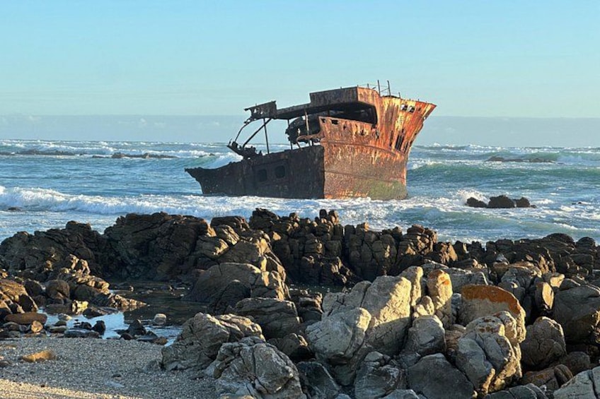 Un pecio oxidado en la orilla rocosa, con olas rompiendo contra él. 1