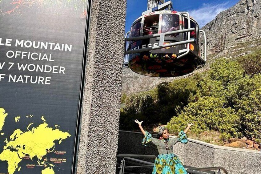 A cable car with passengers, a person in a traditional dress, and a sign about the Table Mountain. 5