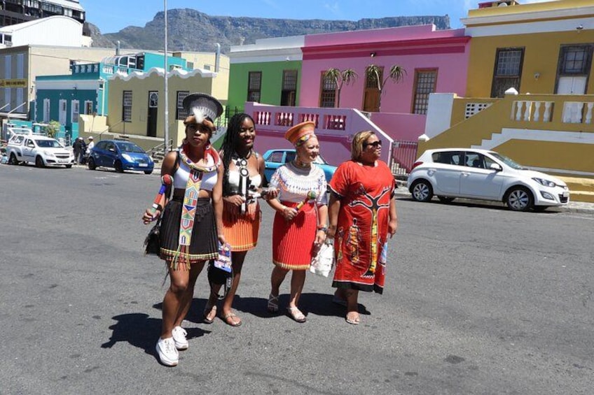 Four people in colorful traditional attire standing in a parking lot with buildings in the background. 5
