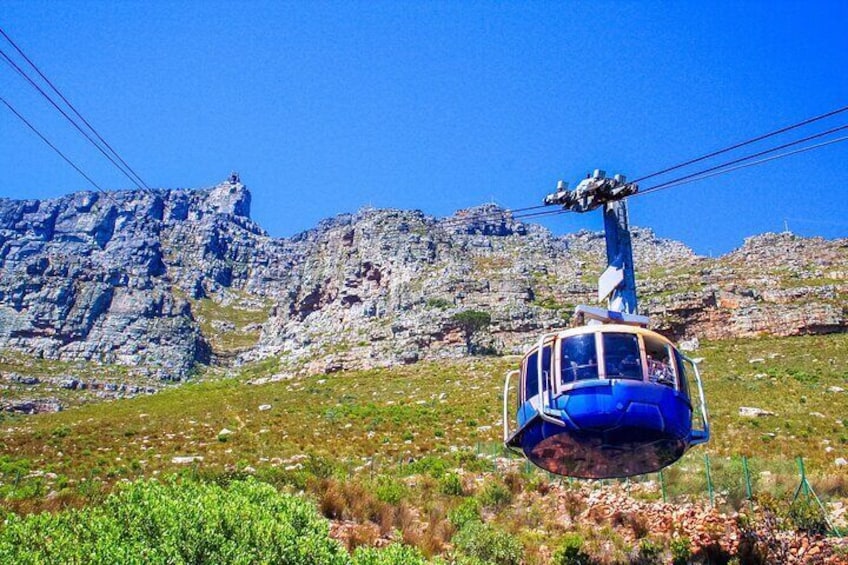 A blue cable car ascending a mountain with rocky terrain and sparse vegetation. 2