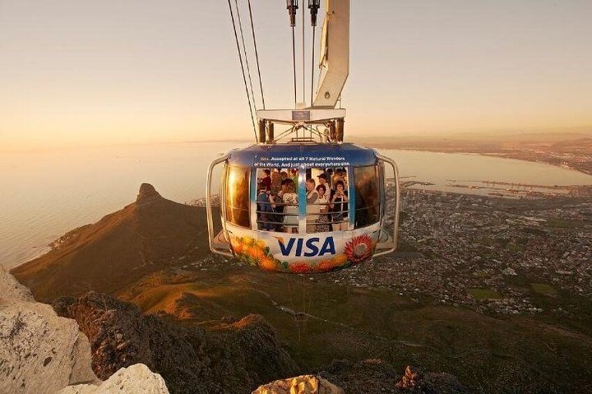 A cable car with 'VISA' branding, suspended over a landscape with a body of water and a city below. 4