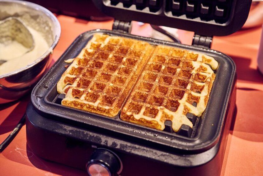 Una plancha para gofres con dos gofres dentro, un tazón de masa y una cuchara. 5