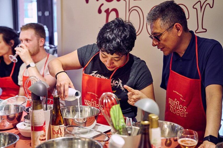 Des personnes portant des tabliers rouges sur lesquels est inscrit « gaufres et bière », préparent des plats derrière un comptoir équipé de divers ustensiles de cuisine et d’ingrédients. 5