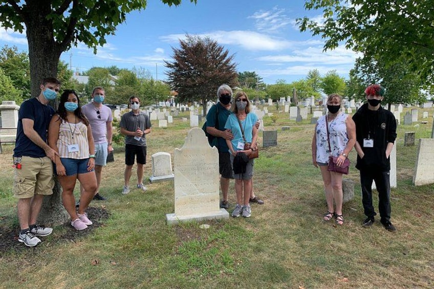Un gruppo di persone in un cimitero, con lapidi e un grande albero sullo sfondo. 3