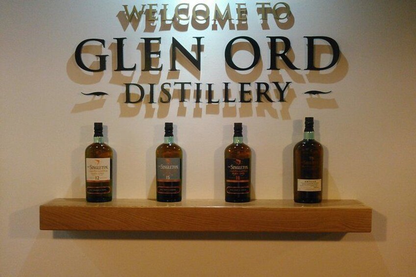 A sign welcoming visitors to Glen Ord Distillery with four bottles of whisky displayed on a shelf. 5