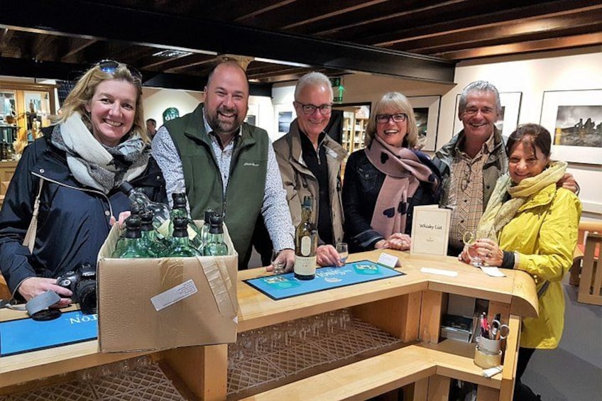 A group of people at a wine tasting event with bottles and glasses on a wooden table. 4