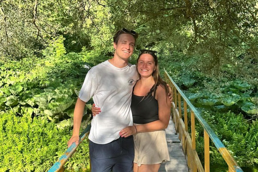 Deux personnes se tiennent sur un pont de bois, entourées de verdure. 3