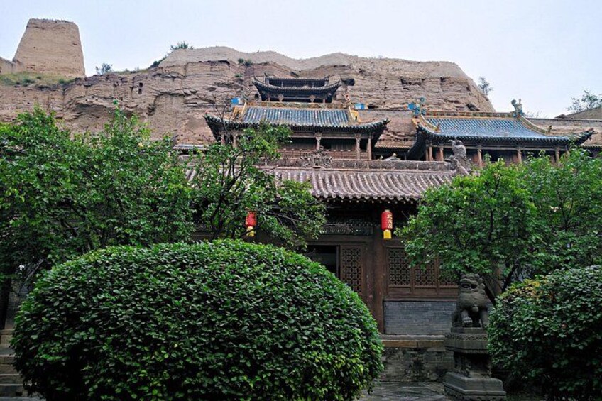 A traditional Chinese building with ornate roofs, surrounded by lush greenery and a rocky hill in the background. 4
