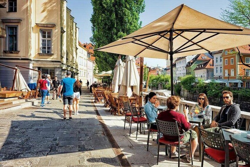 Una calle empedrada con mesas al aire libre, gente caminando y edificios al fondo. 2