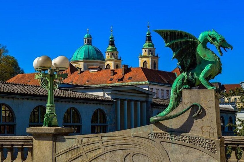 Eine grüne Drachenstatue auf einer Brücke, ein Gebäude mit grünen Kuppeln und ein Glockenturm. 1