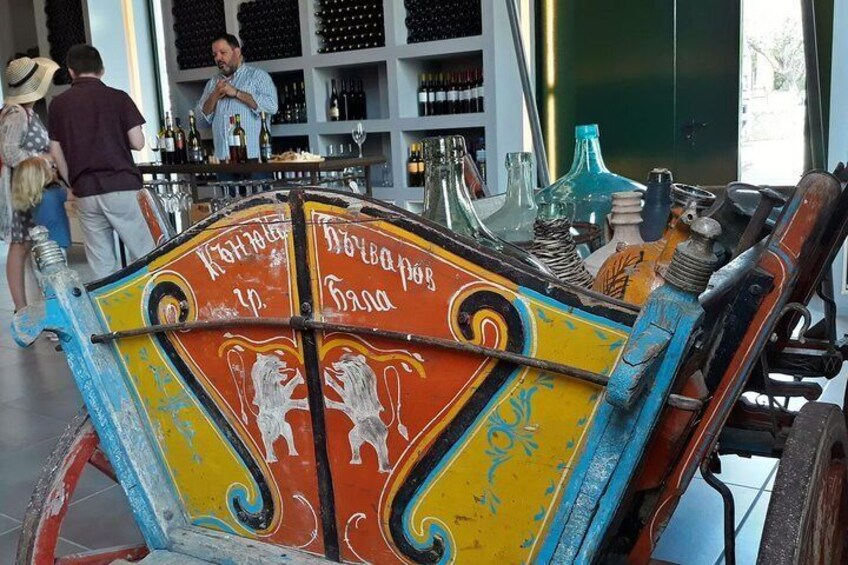 A colorful, ornate cart with decorative elements and text, placed in a bar setting with shelves of bottles in the background. 2