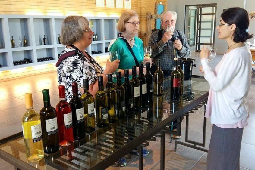 A wine tasting event with several people standing around a table filled with wine bottles. 3