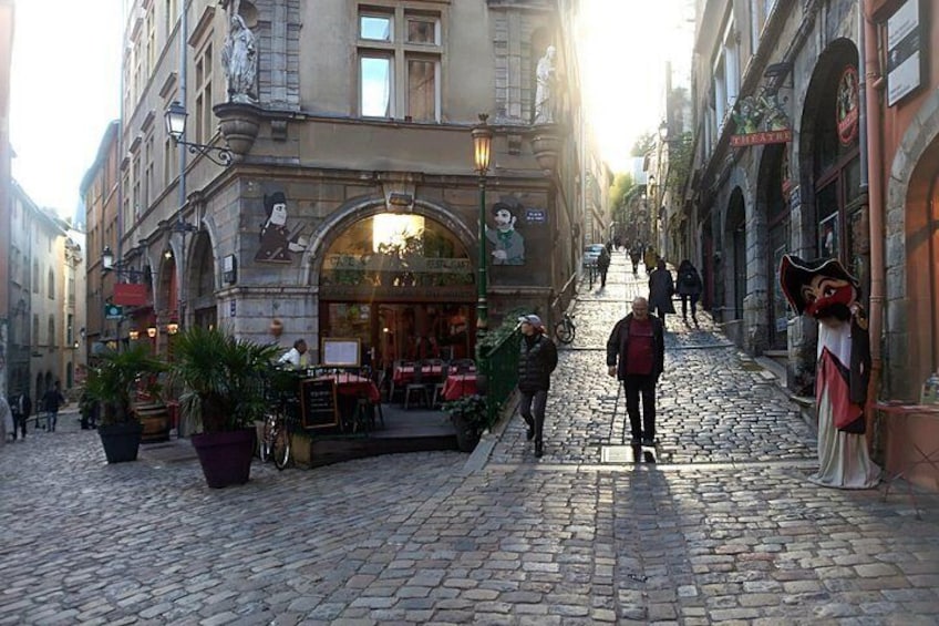 Una strada acciottolata con un caffè, piante in vaso e una statua. 5