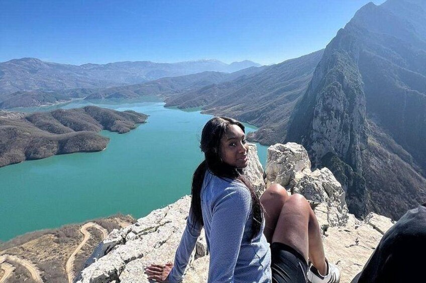 A person sitting on a rocky outcrop overlooking a turquoise lake surrounded by mountains. 2