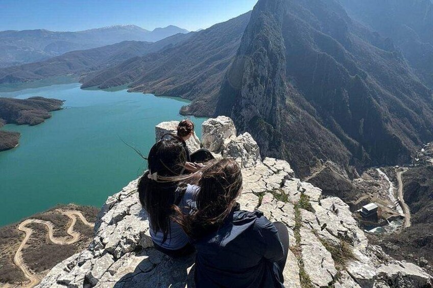 A mountainous landscape with a lake, rocky terrain, and a person sitting on a ledge. 4