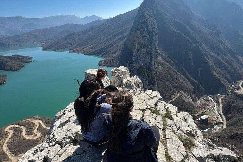 A group of people sitting on a rocky outcrop overlooking a lake and mountains. 3