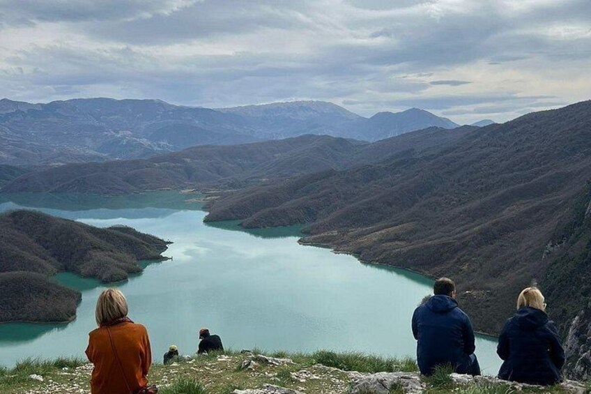 A group of people sitting on a mountain overlooking a lake surrounded by hills. 5