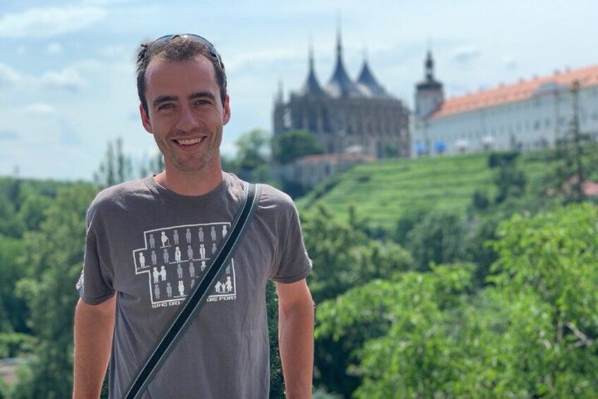 Una persona de pie frente a un castillo, con un paisaje verde al fondo. 1