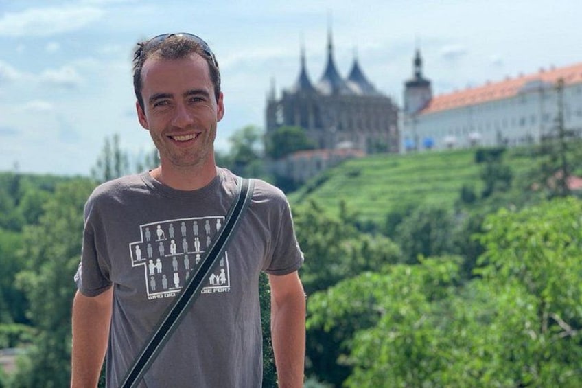 Une personne se tient devant un château, avec des collines verdoyantes en arrière-plan. 1