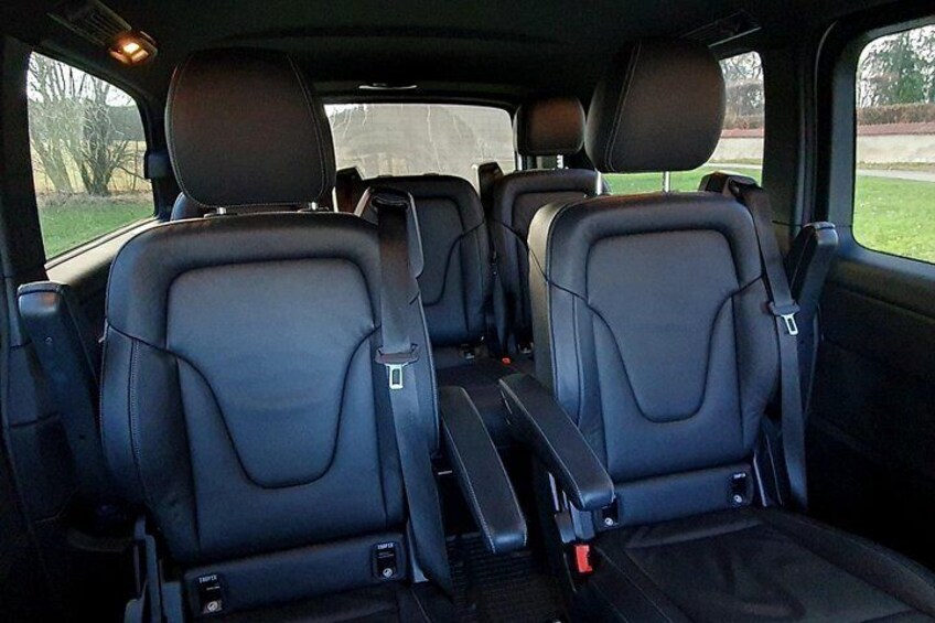A vehicle interior with three rows of seats, seat belts, and a center console. 2