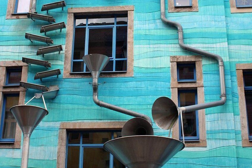 Un bâtiment à la façade bleue, doté de nombreuses fenêtres et orné de diverses structures métalliques fixées à l’extérieur. 3