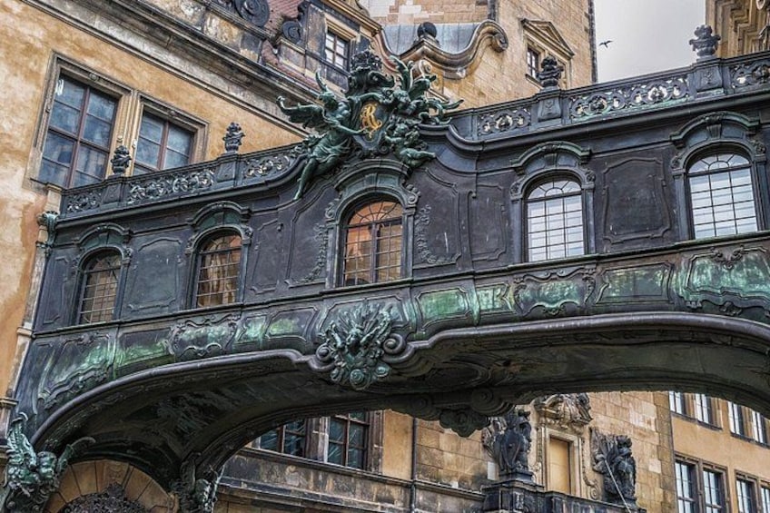 Un pont métallique orné, doté de motifs complexes et de statues, qui se détache sur la façade d’un bâtiment historique. 5