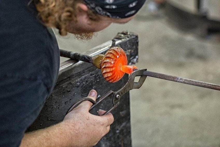 A person working with a glass blower's tool, shaping molten glass. 3