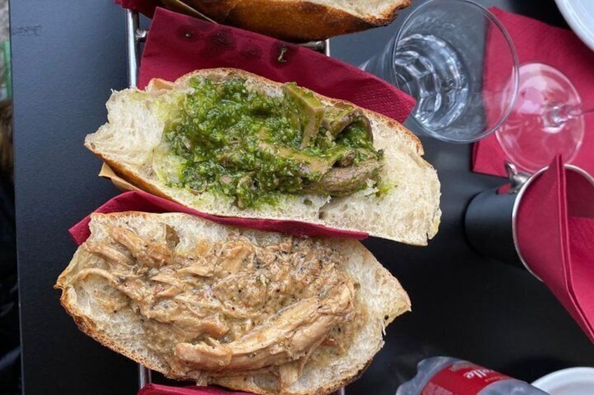 Een boterham met groene saus en geraspeld vlees op een tafel met een rode servet en een glas water. 3