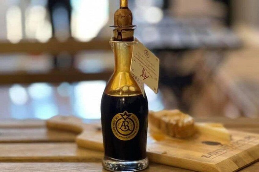Una botella de líquido oscuro con tapa dorada y una etiqueta, sobre una superficie de madera con fondo desenfocado. 2
