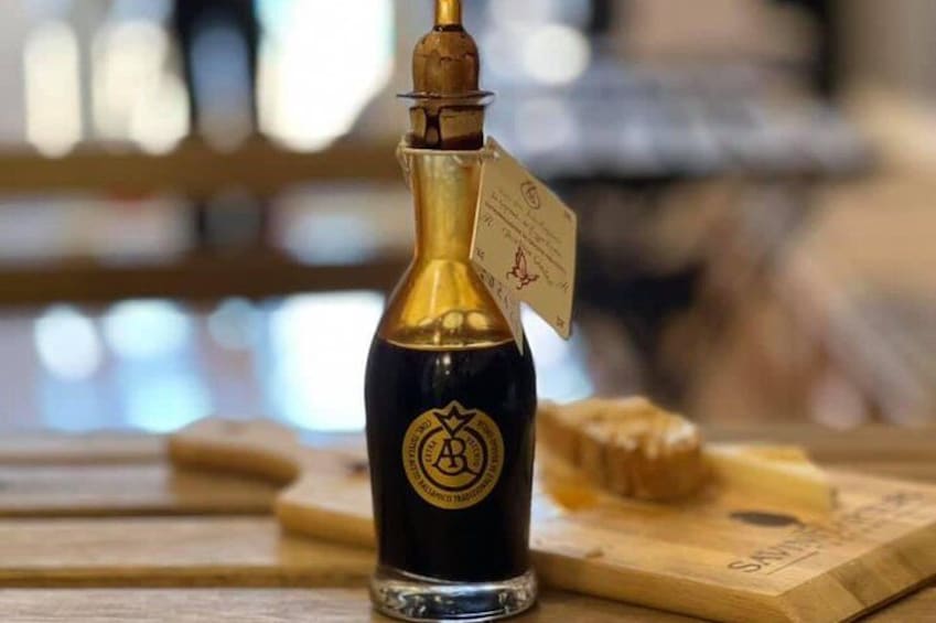 A bottle of dark liquid with a gold label and a tag, placed on a wooden surface with a blurred background. 2