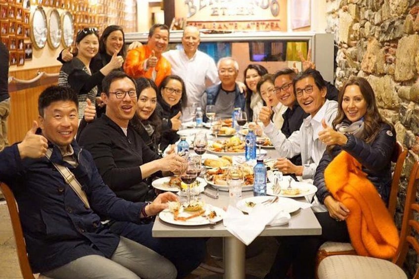 A group of people sitting around a table with food and drinks, in a restaurant with a stone wall background. 5